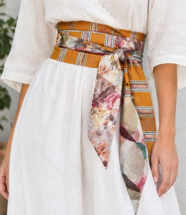 Fajín Sinvergüenza de rayas ocre y estampado floral anudado a la cintura sobre vestido blanco